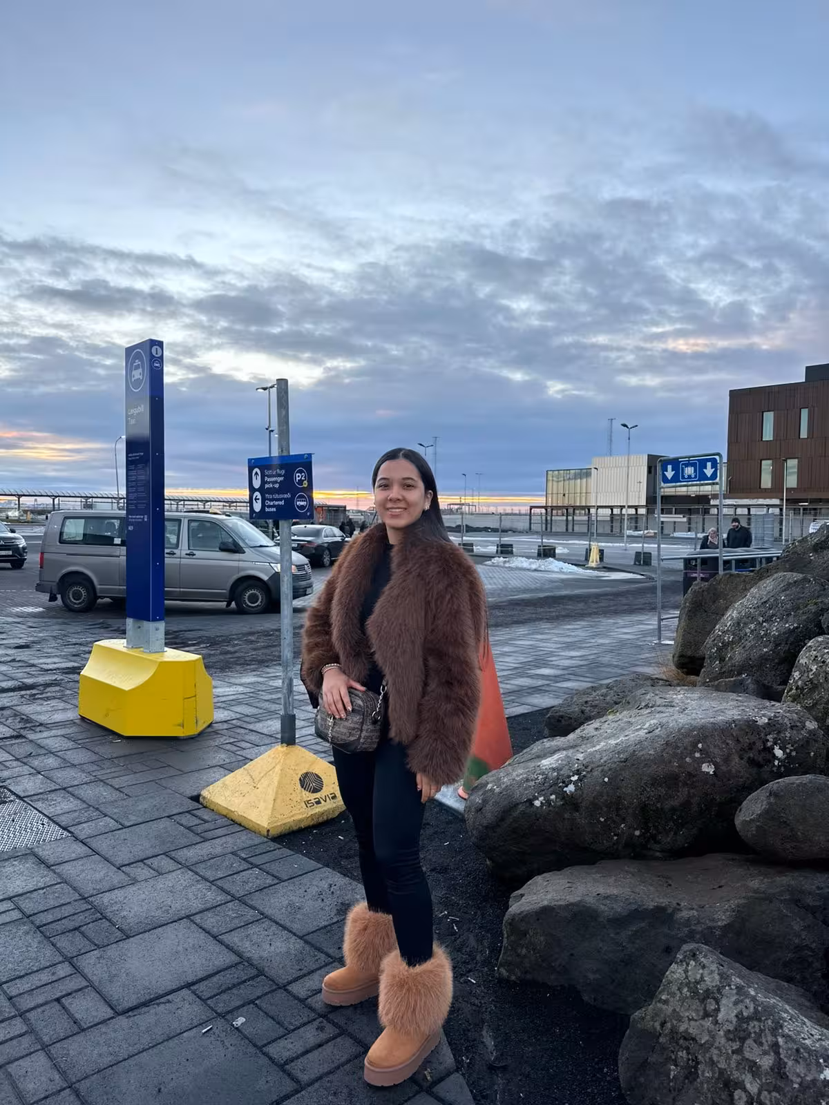 Traveler in fur coat and boots outside Reykjavik KEF Airport departure area with parking signs