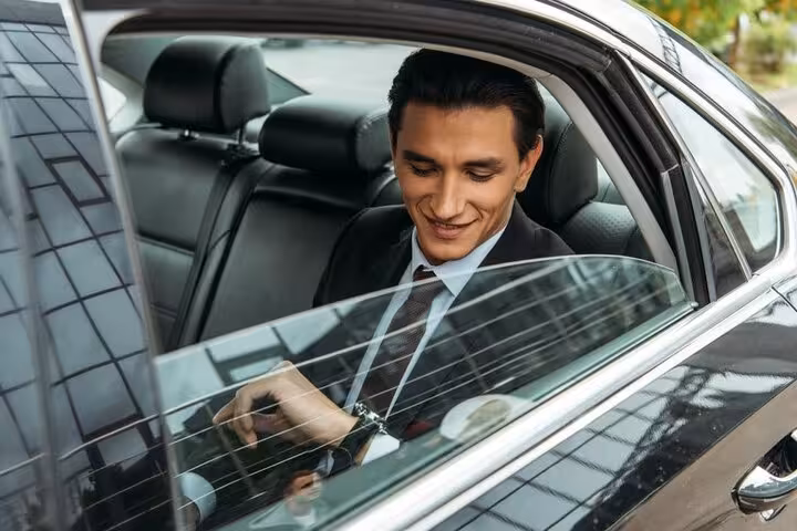 Businessman in suit smiling while seated in luxury black car backseat during private airport transfer