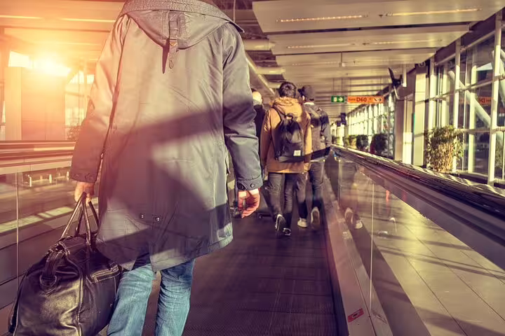 Travelers walking with luggage on airport moving walkway toward departure gates in Keflavik Airport