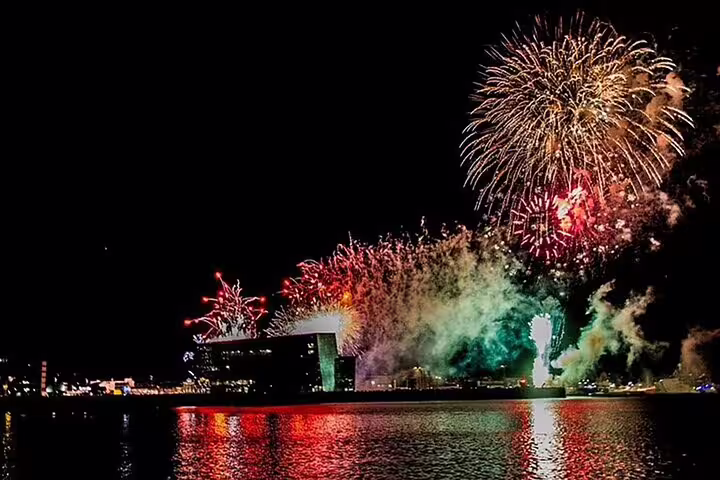 Colorful New Year Eve fireworks exploding over Reykjavik harbor waterfront reflected on calm water at night