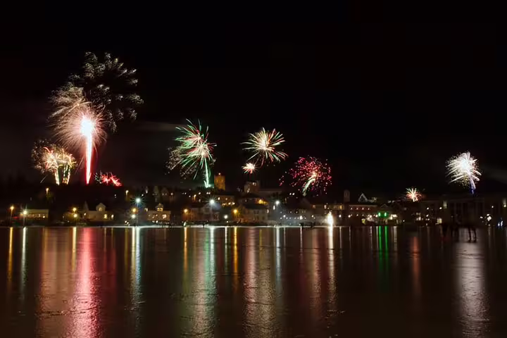 Colorful New Year fireworks over Reykjavik harbor waterfront reflecting on calm water at night