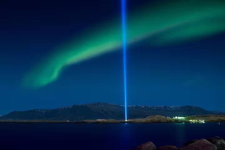 Aurora borealis and blue light beam over Reykjavik bay at night with mountain backdrop