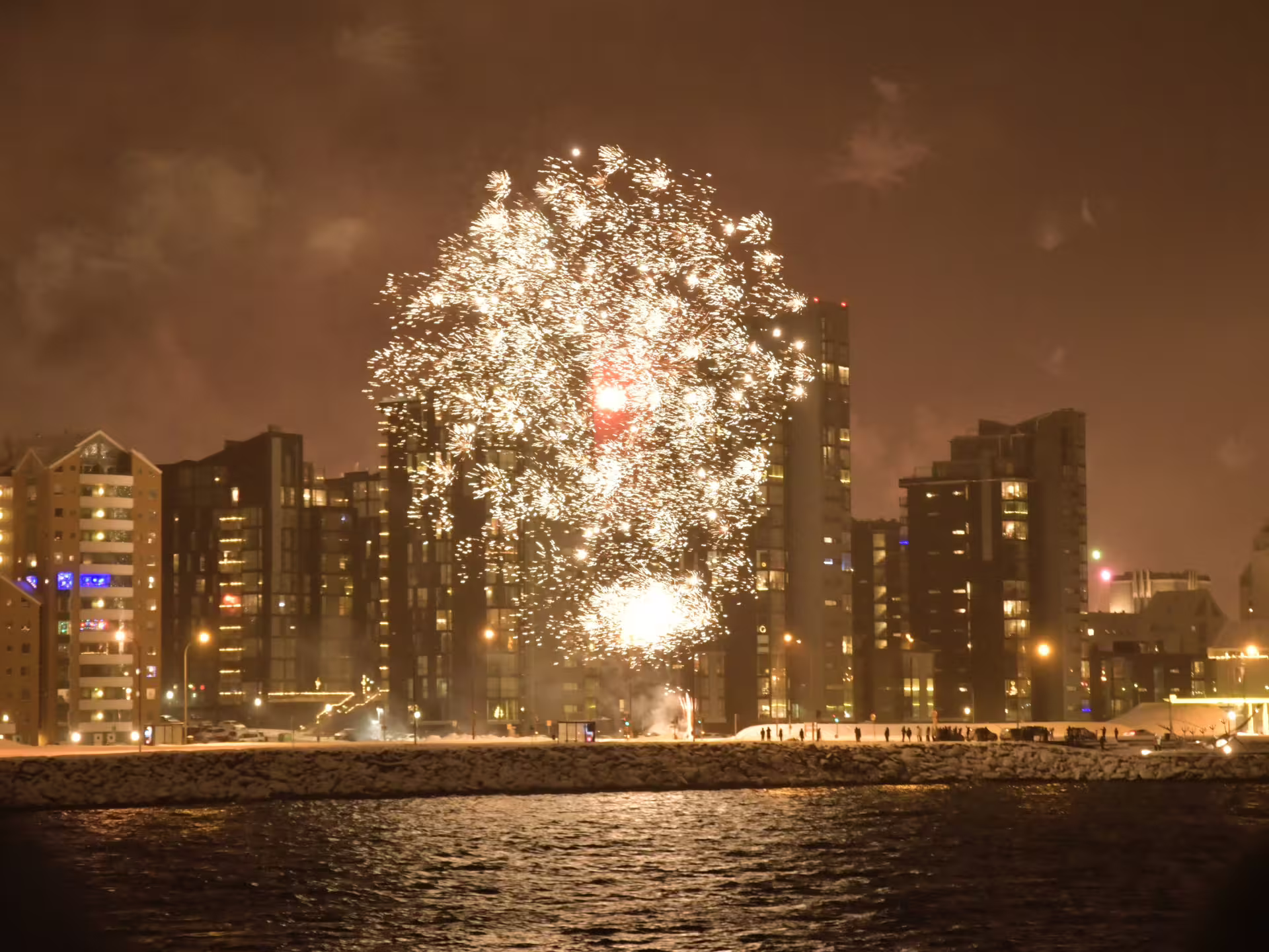 Brilliant fireworks exploding over Reykjavik waterfront buildings at night during New Year's Eve celebrations