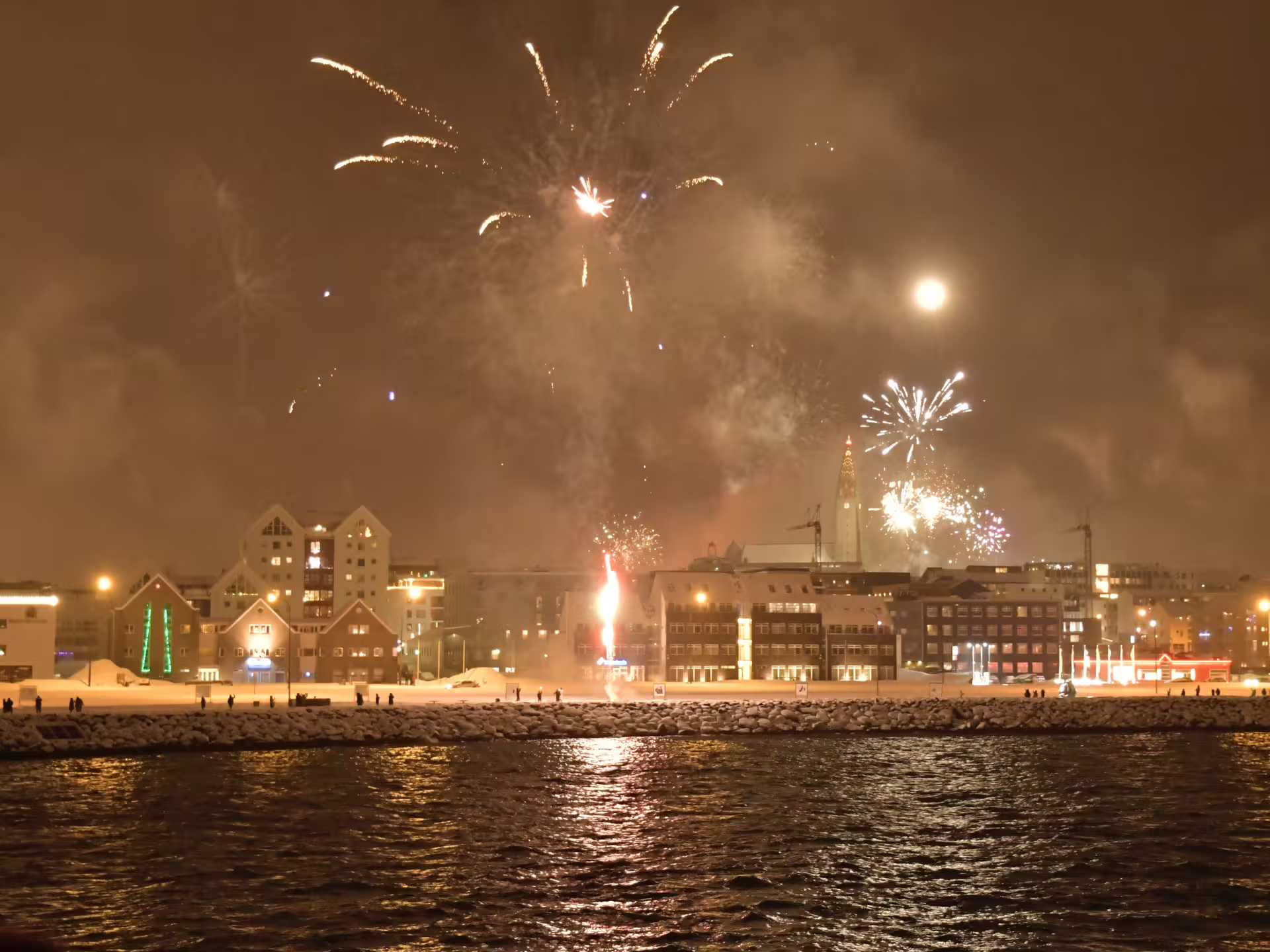 Reykjavik New Year's Eve fireworks over the city waterfront viewed from the sea at night