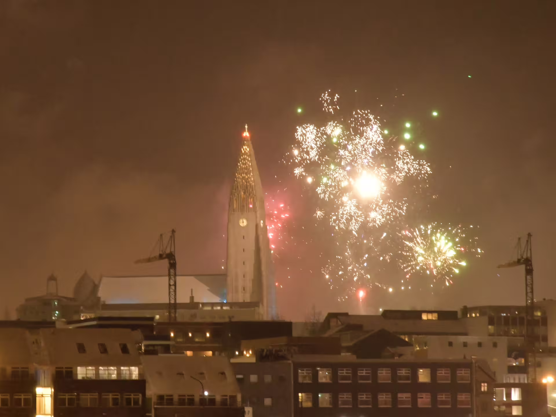 Reykjavik New Year's Eve fireworks exploding over city skyline with Hallgrímskirkja church lit up at night