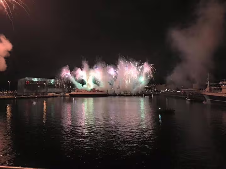 Colorful New Year's Eve fireworks bursting over Reykjavik harbor at night, reflected in calm water