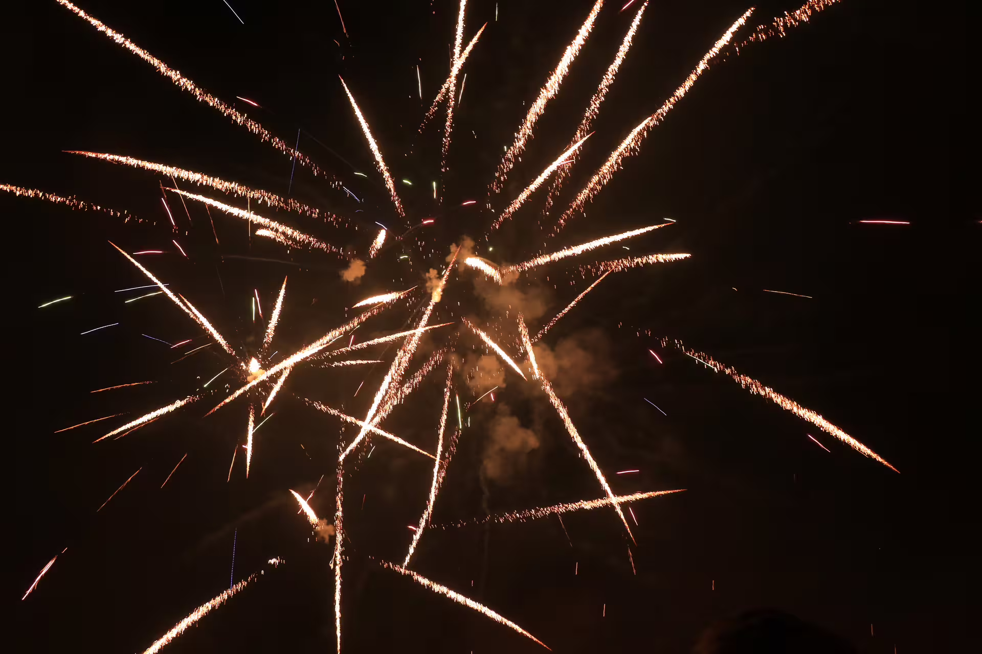 Golden fireworks exploding against dark night sky with sparks and smoke trails