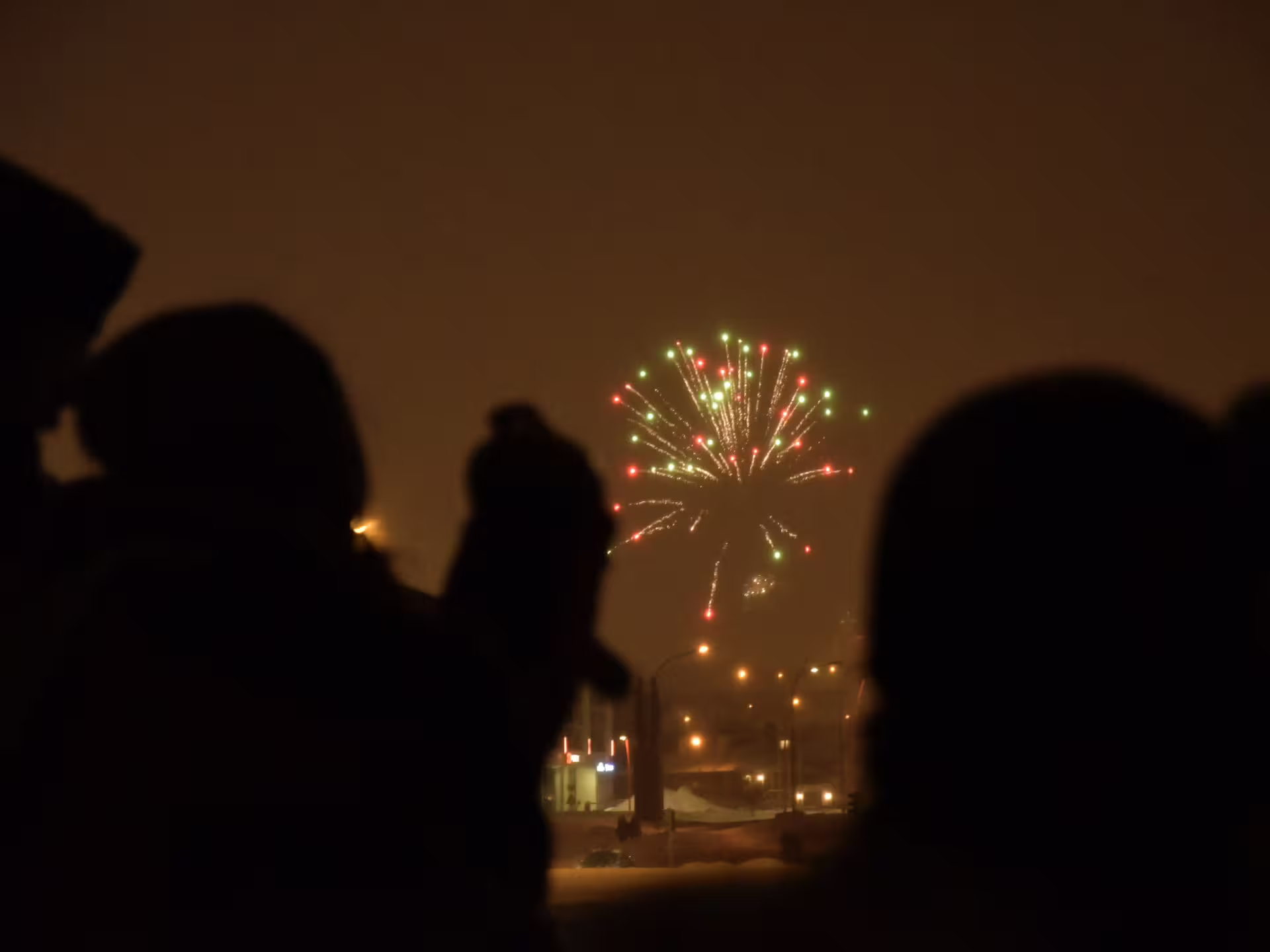 Silhouettes of people watching red and green New Year's Eve fireworks burst over Reykjavik night sky