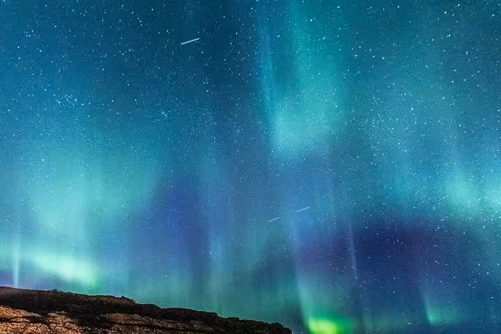 Vivid green and blue aurora borealis dancing over rocky Reykjavik landscape on a starry night