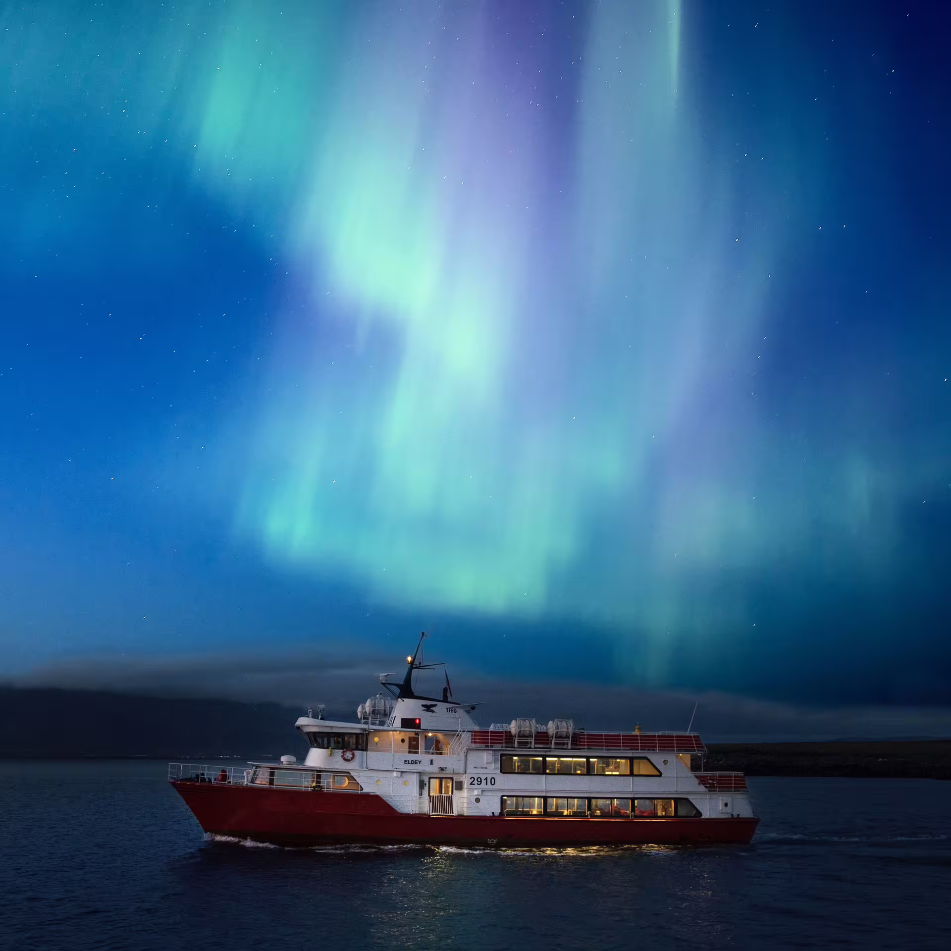 Eldey boat cruise on calm waters under vibrant green and purple northern lights in Reykjavik night sky