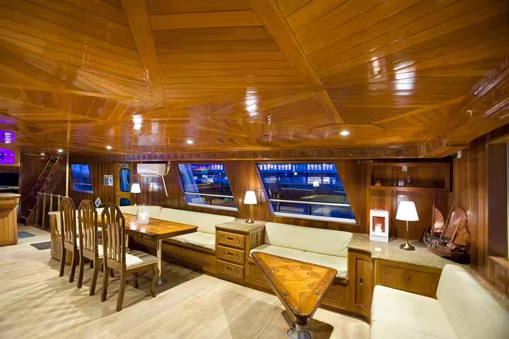 Elegant wooden interior of a night cruise boat with dining area, lounge seating, and panoramic windows