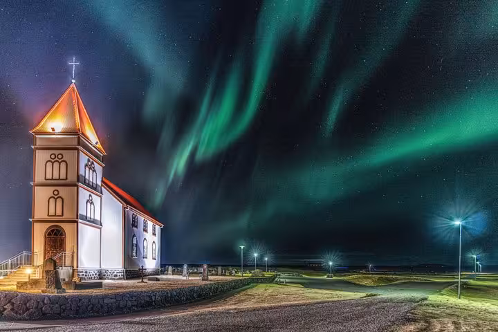 Northern lights dancing over illuminated white church with red roof in Reykjavik, Iceland at night