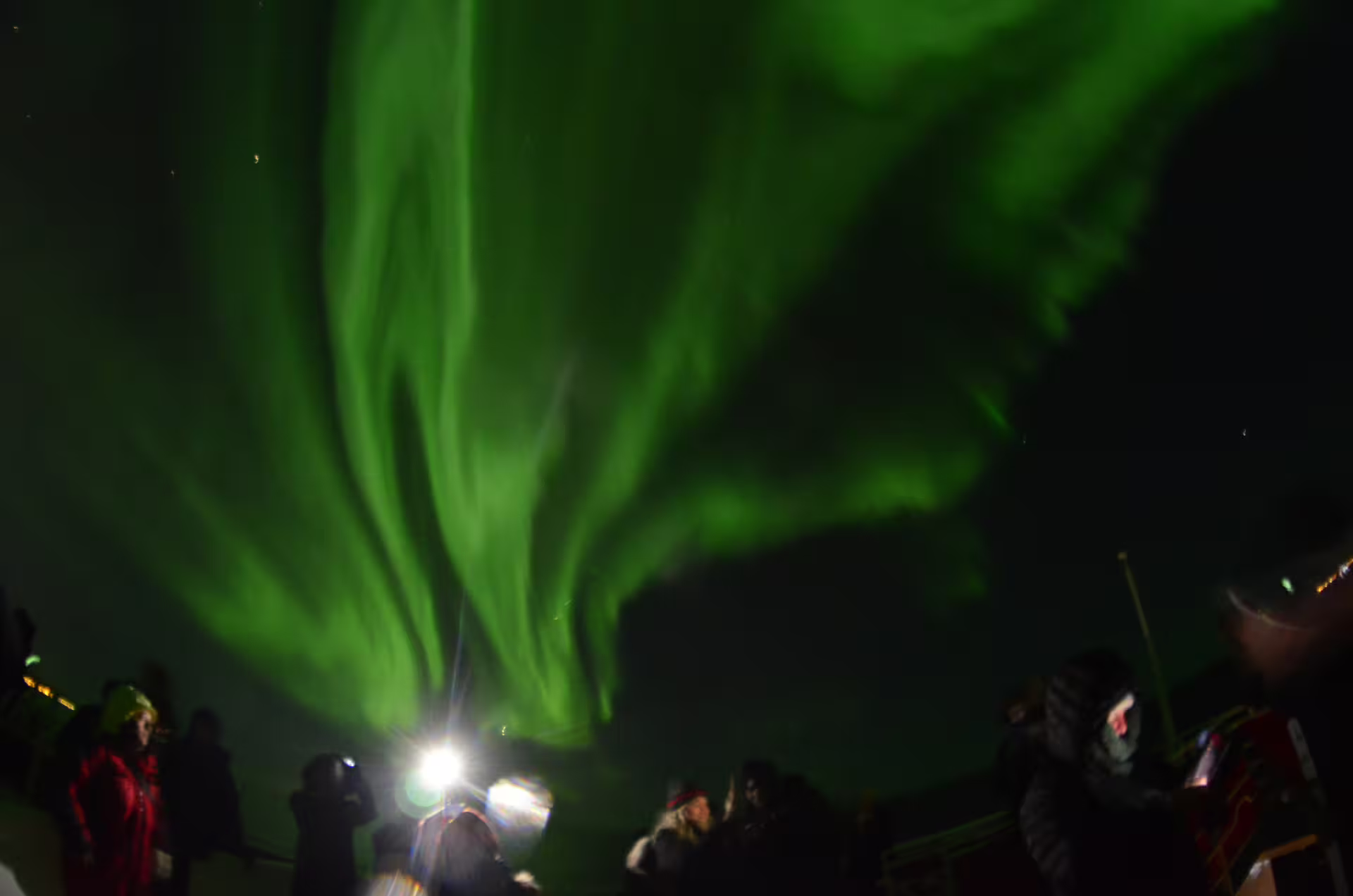 Tourists watching vibrant green northern lights aurora borealis dance across night sky in Reykjavik
