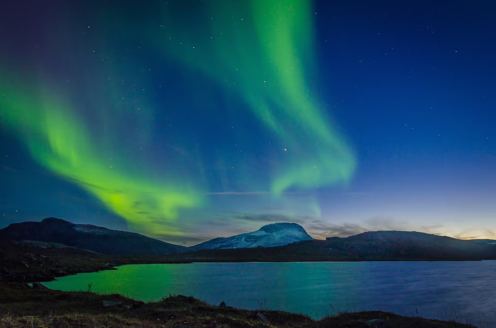Vibrant green northern lights dancing over a calm lake with snow-capped mountains in Iceland