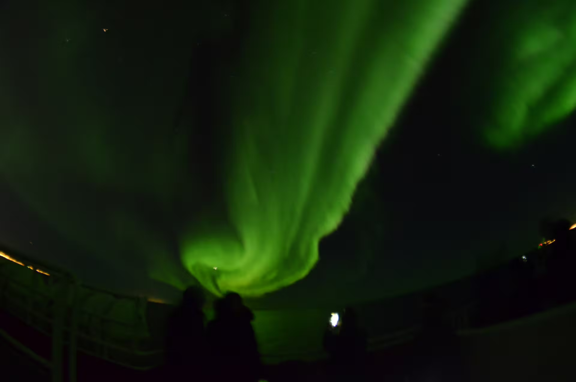 Two silhouettes watching vivid green northern lights swirling across the night sky in Reykjavik
