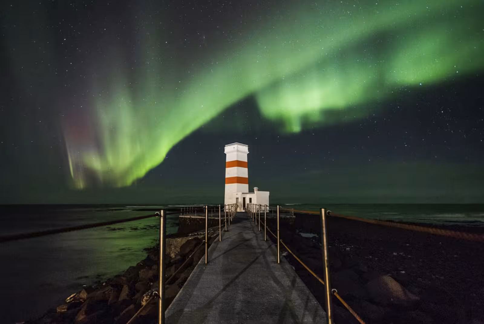 Northern lights aurora borealis dancing over a red and white striped lighthouse in Reykjavik, Iceland at night