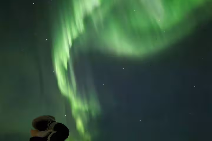 Vibrant green northern lights swirling over Reykjavik with a person gazing up at the aurora borealis