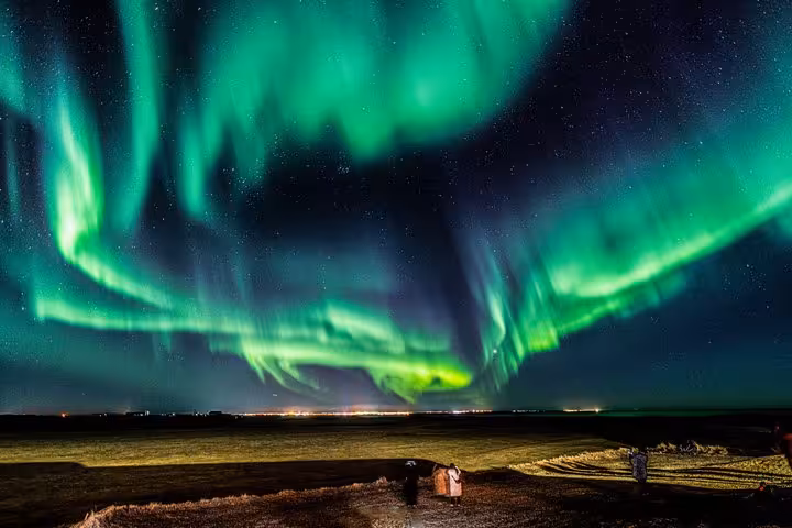Vibrant green northern lights aurora borealis over flat Icelandic landscape with two spectators at night