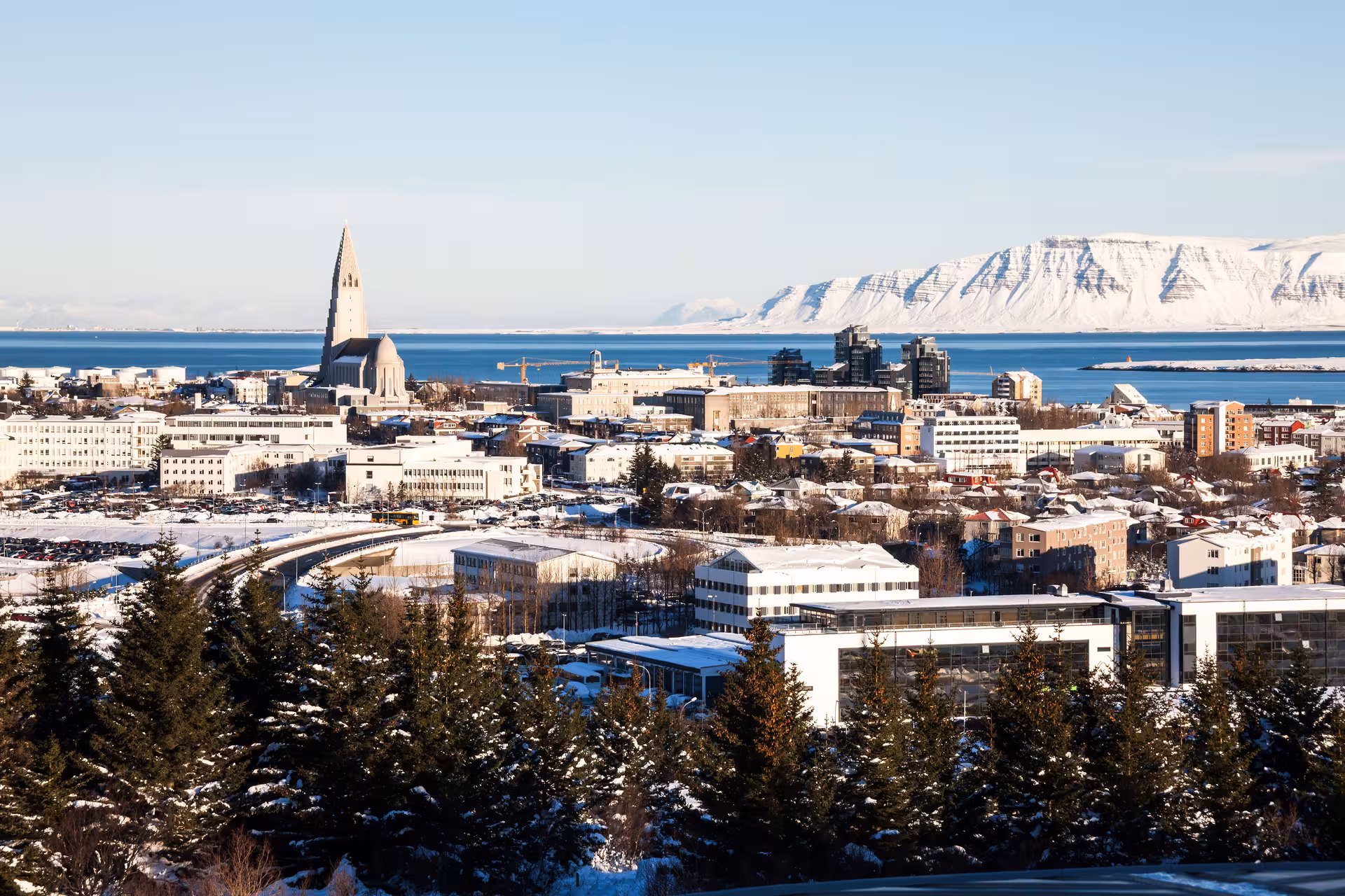 Daytime panorama of Reykjavík with snow-capped buildings and mountains, highlighting a stunning Northern Lights destination.