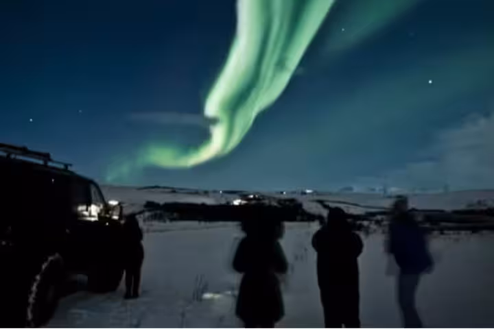 Tourists watching vibrant green northern lights aurora borealis over snowy Reykjavik landscape at night