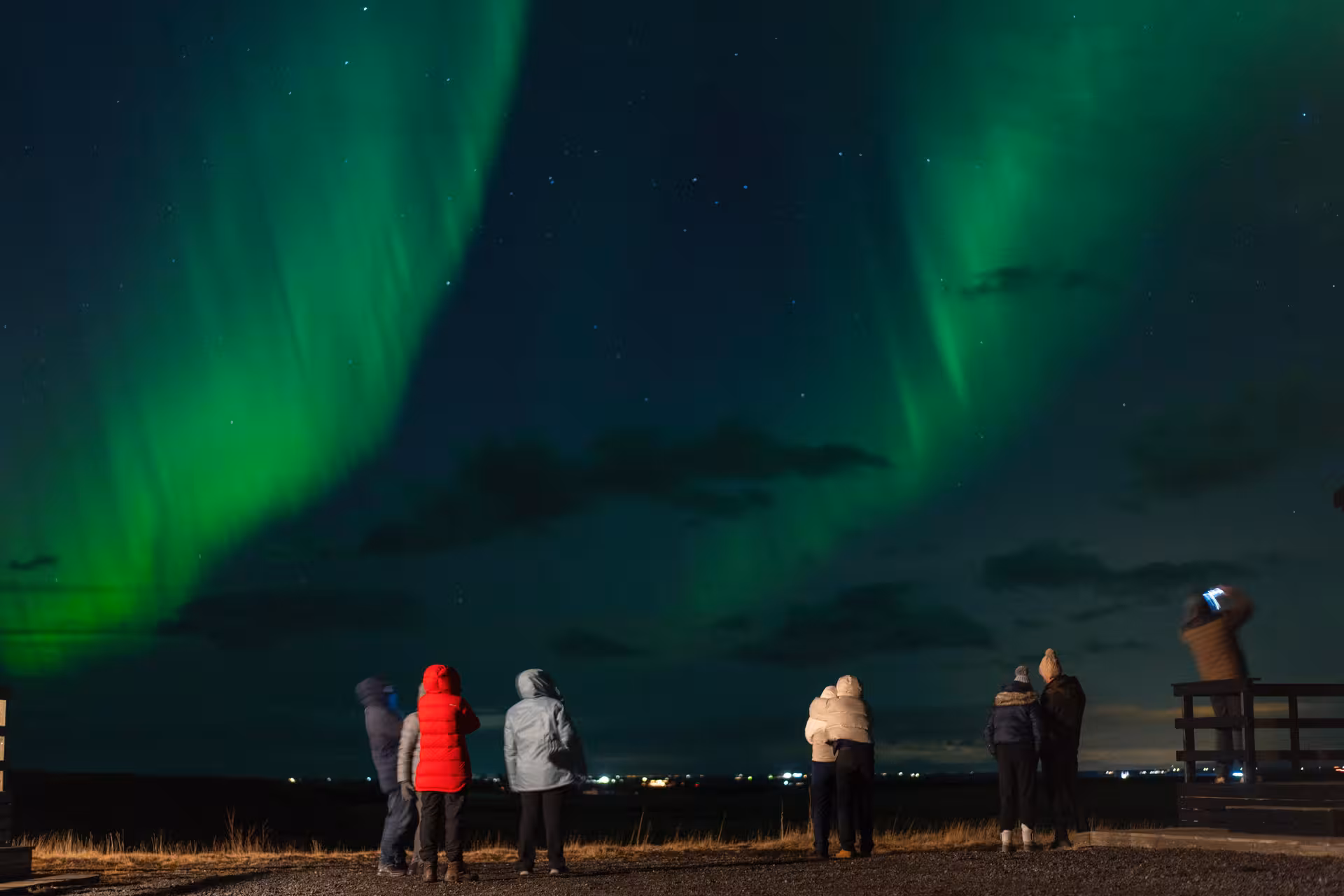 Group of tourists watching vibrant green northern lights aurora borealis over Reykjavik night sky