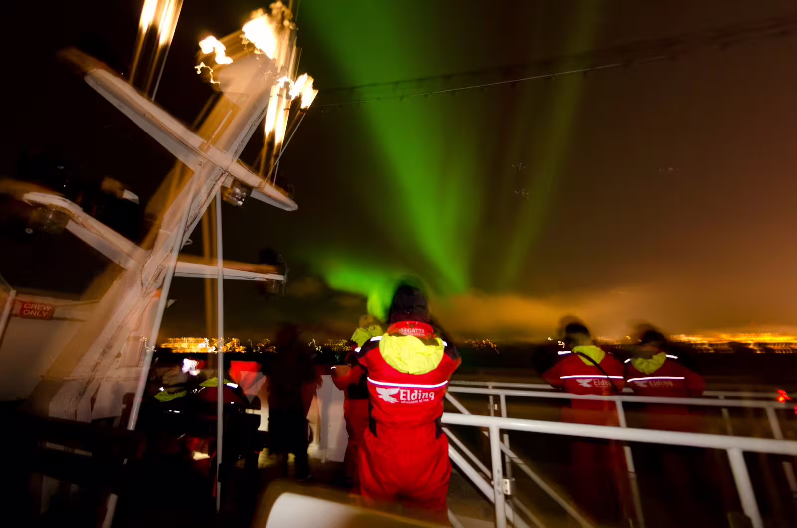 Elding tour guides and passengers on boat deck watching vivid green northern lights over Reykjavik at night