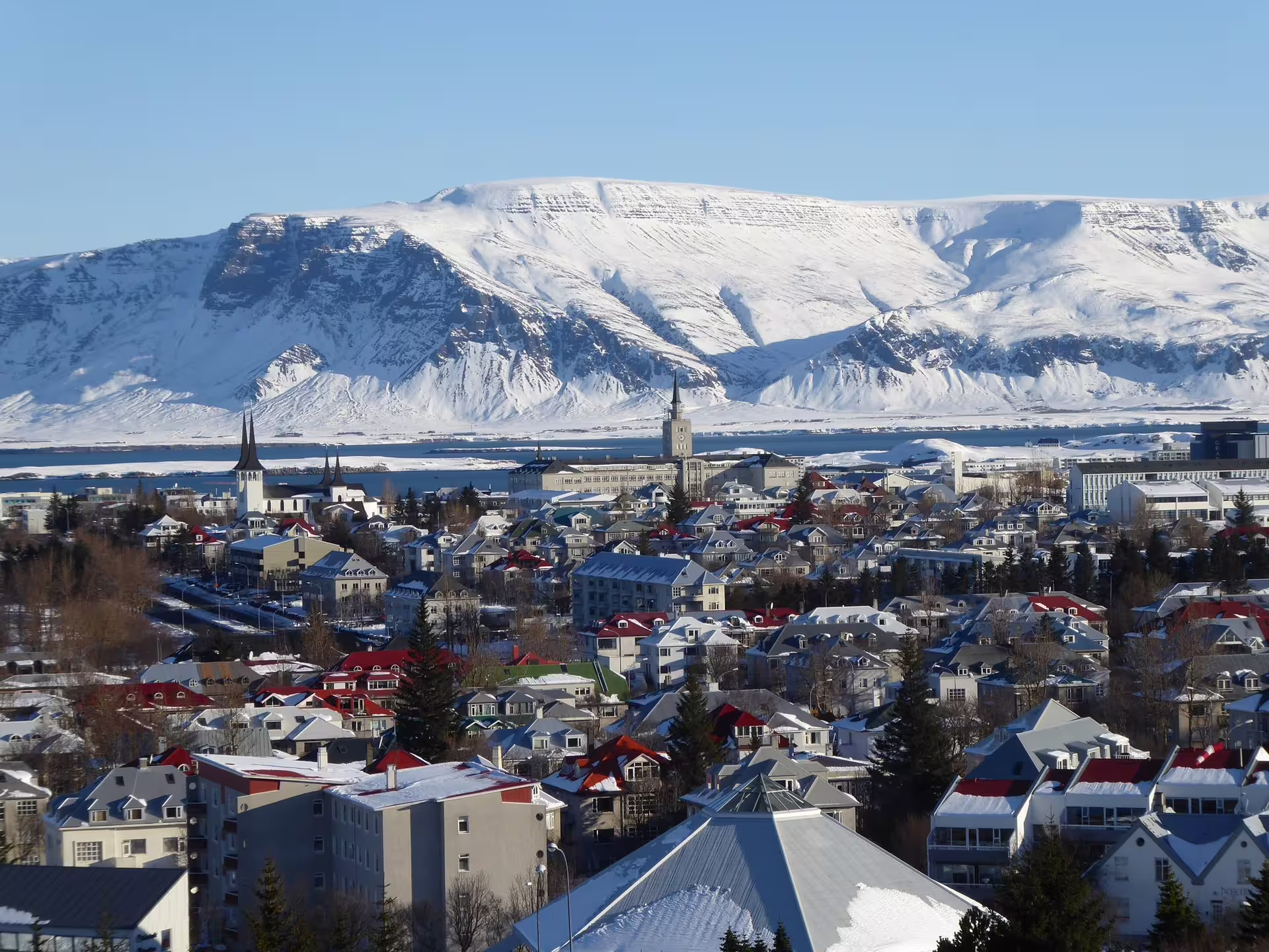 Panoramic winter view of Reykjavik cityline with snow-covered mountains and fjord in background