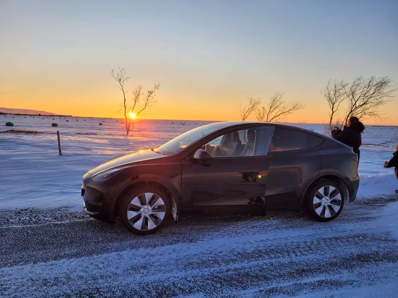 Private Reykjavik city tour Tesla SUV parked on snowy landscape during golden sunset in Iceland winter