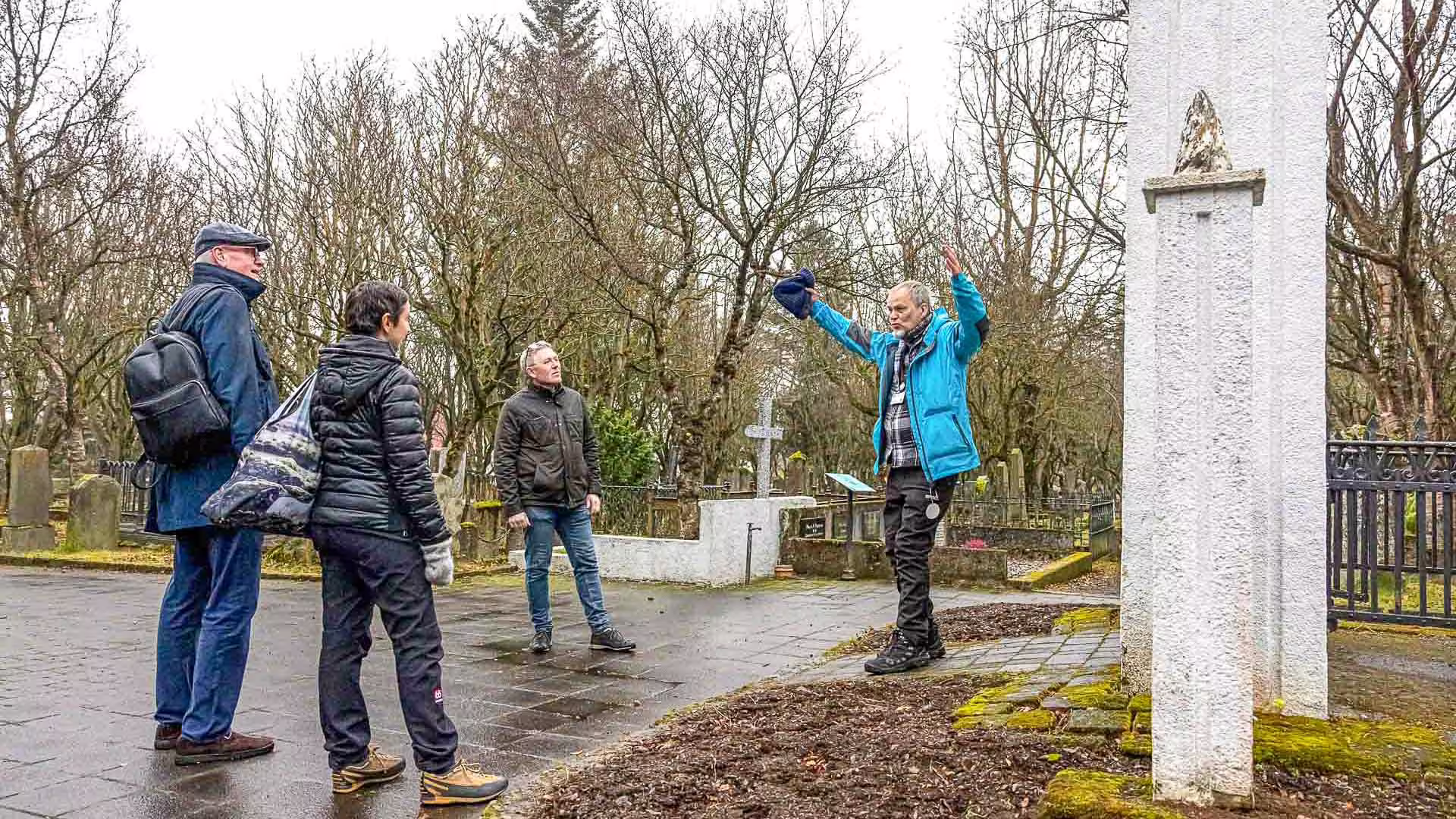 Tour guide gesturing at historic monument in Reykjavik cemetery with three visitors on walking tour