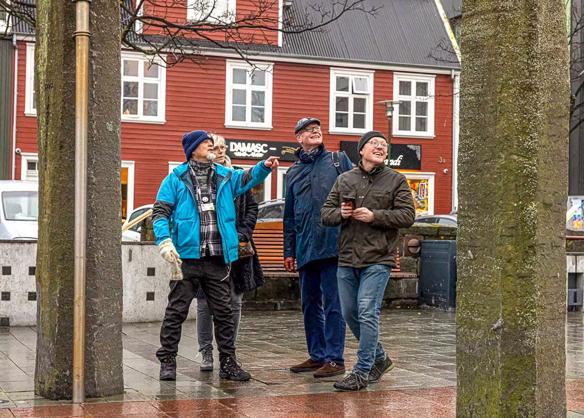 Tour guide pointing out city highlights to smiling tourists on a rainy Reykjavik walking tour