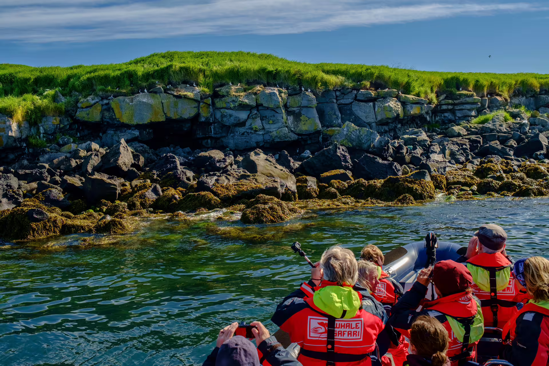 Whale Safari tourists in red life jackets on inflatable boat near rocky seabird island in Reykjavik bay