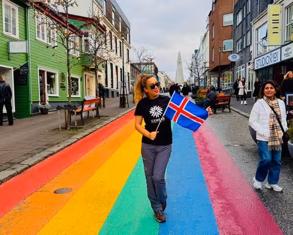 Vibrant street scene in Reykjavik with a rainbow road and a person holding an Icelandic flag, capturing local culture.
