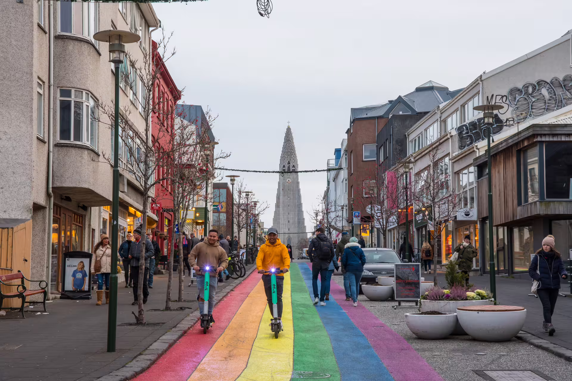 Rainbow street in Reykjavik with Hallgrímskirkja church in background and people on scooters