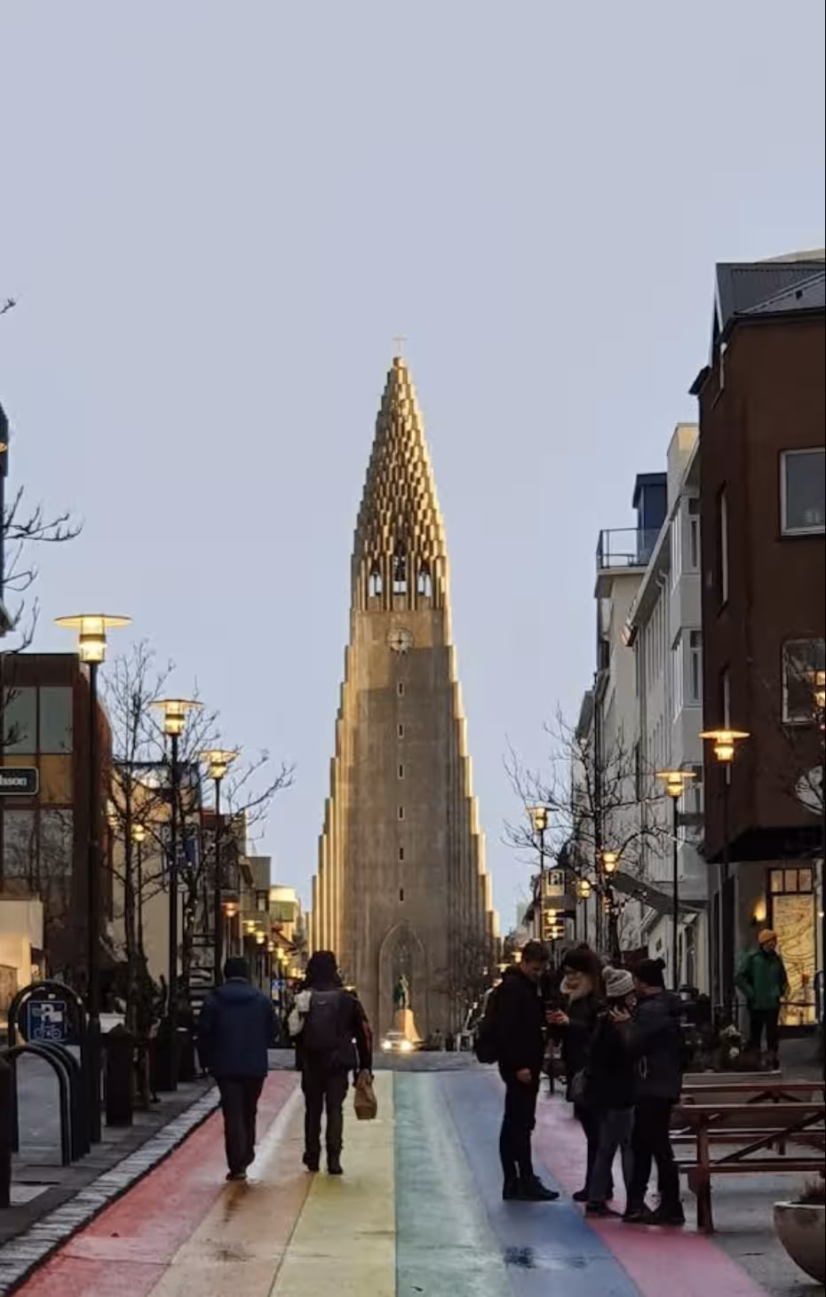 Rainbow street leading to Hallgrímskirkja church in Reykjavik with pedestrians walking at dusk