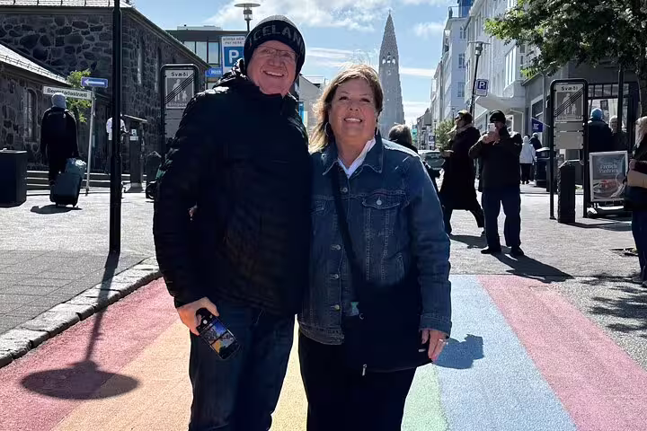 Couple smiling on rainbow crosswalk in Reykjavik city center with Hallgrímskirkja church in background