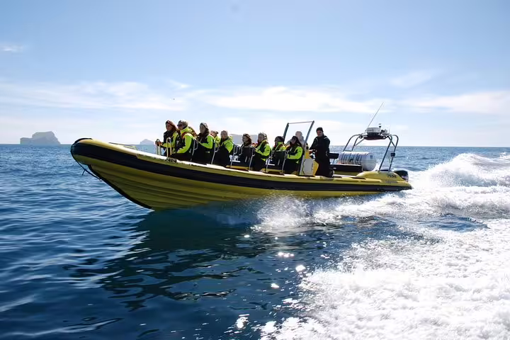 Group of passengers in life jackets riding a yellow RIB speedboat on calm blue ocean near Reykjavik