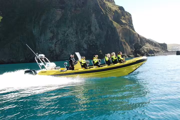 Yellow RIB speedboat with passengers in life jackets speeding through turquoise waters near rocky cliffs in Reykjavik