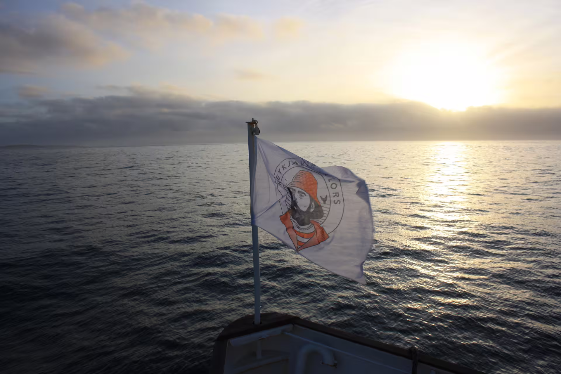 Reykjavik Sailors flag flying from whale watching boat bow at sunset over calm ocean