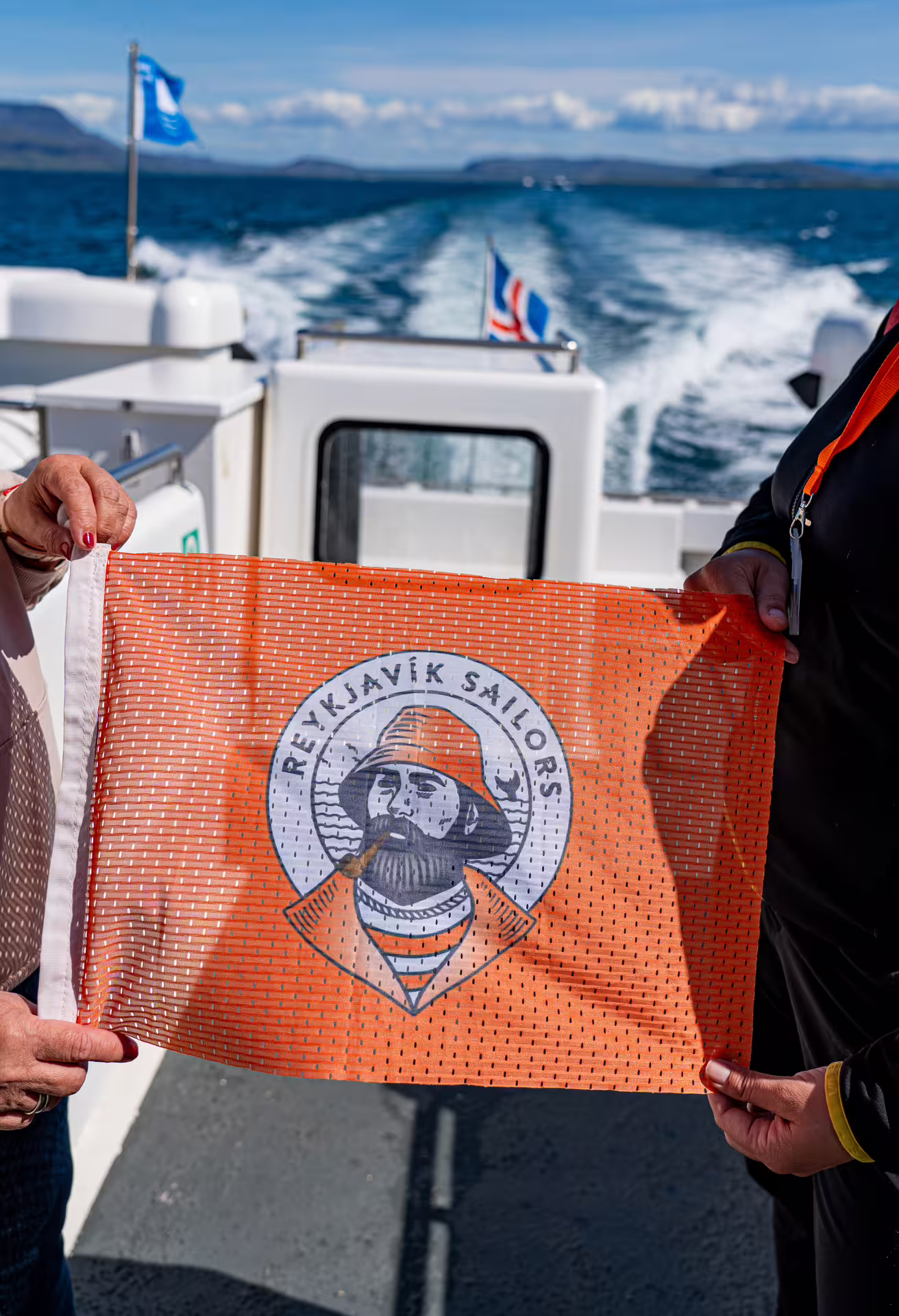Reykjavik Sailors orange flag held on whale watching cruise boat deck with Icelandic flag and ocean wake