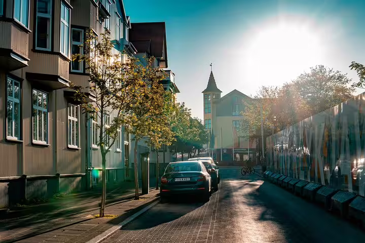 Sunny Reykjavik street with parked car and church tower, ideal for private airport transfer