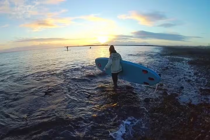 A person carries a paddleboard into the serene waters of Reykjavik at sunset, capturing the beauty of an Icelandic adventure tour.