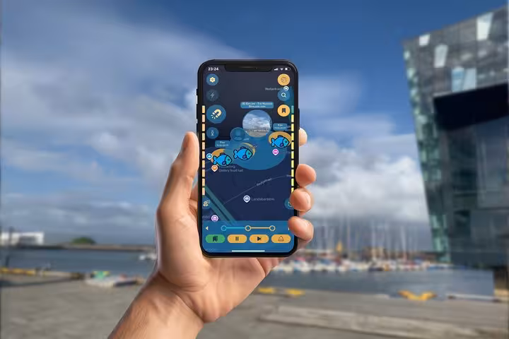 Hand holding smartphone displaying Viking walking tour app with blue fish icons and map of Reykjavik harbor