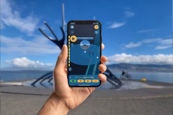 Hand holding smartphone with Viking walking tour app near Sun Voyager sculpture in Reykjavik