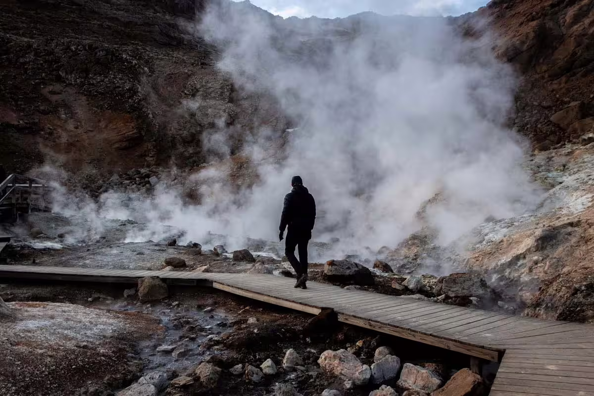Hiker walking on wooden boardwalk through steaming geothermal vents on Reykjanes Peninsula volcano