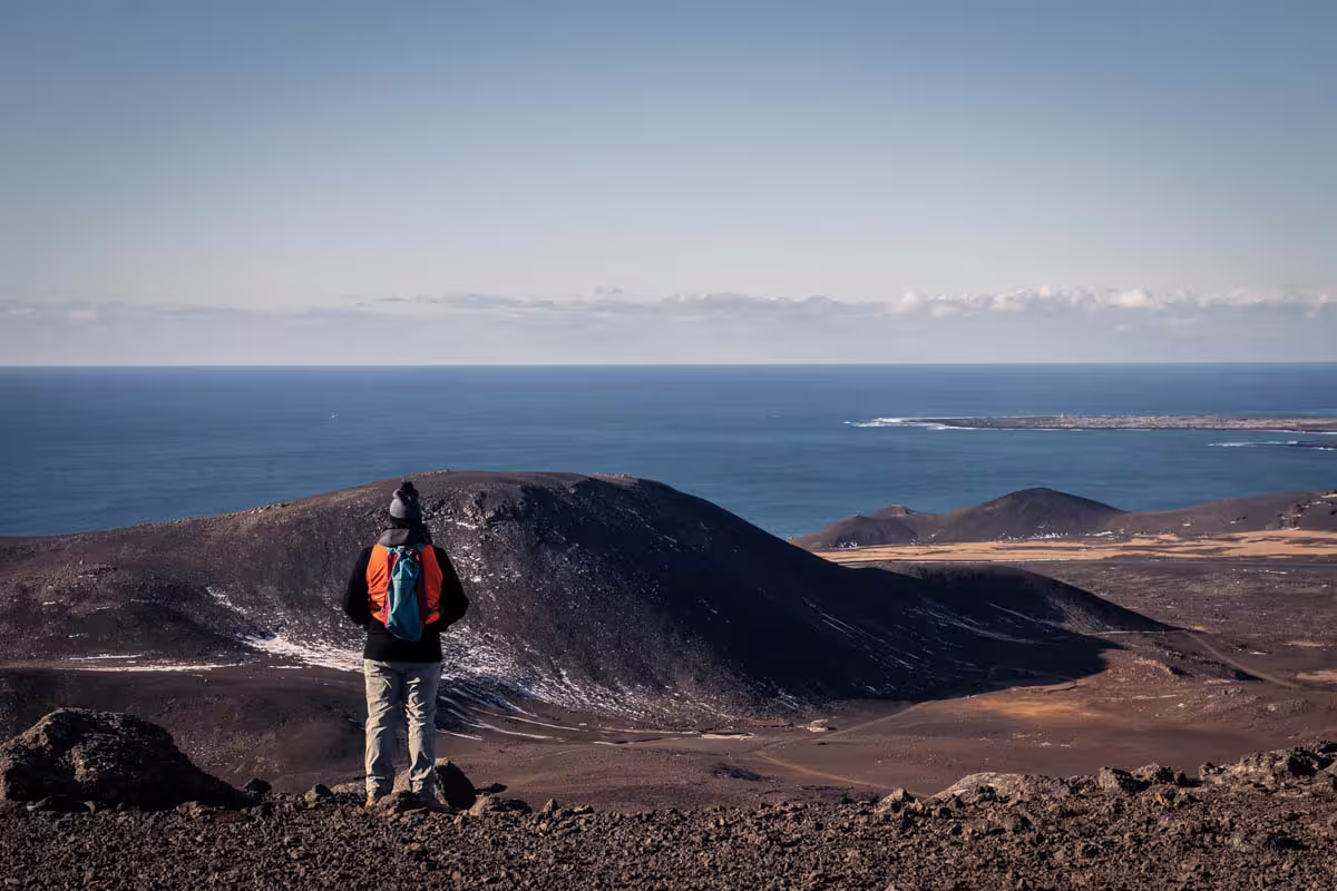 Hiker with backpack overlooking volcanic craters and ocean on Reykjanes Peninsula, Iceland