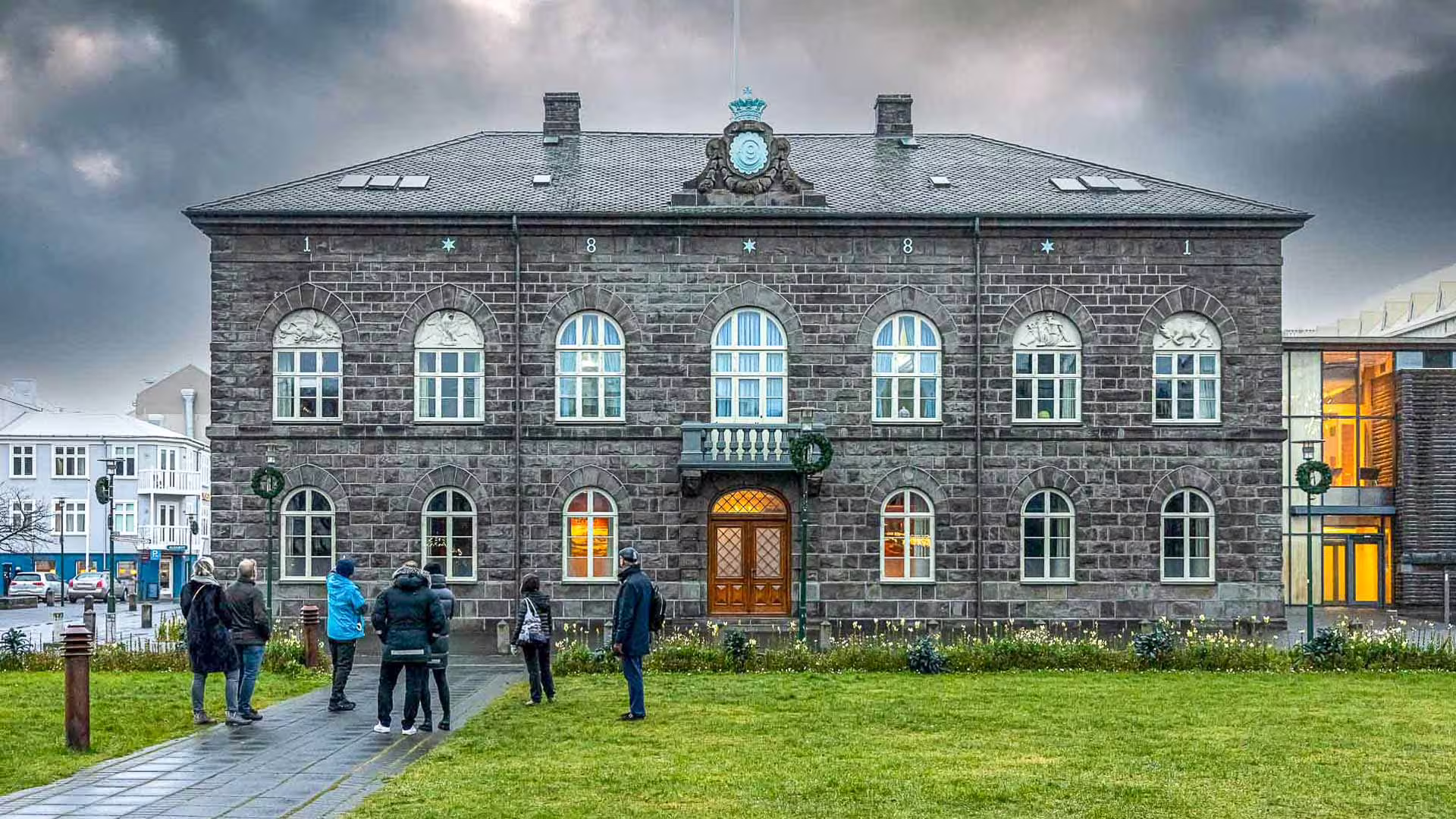 Tourists on walking tour outside Alþingi parliament building in Reykjavik under dramatic cloudy sky