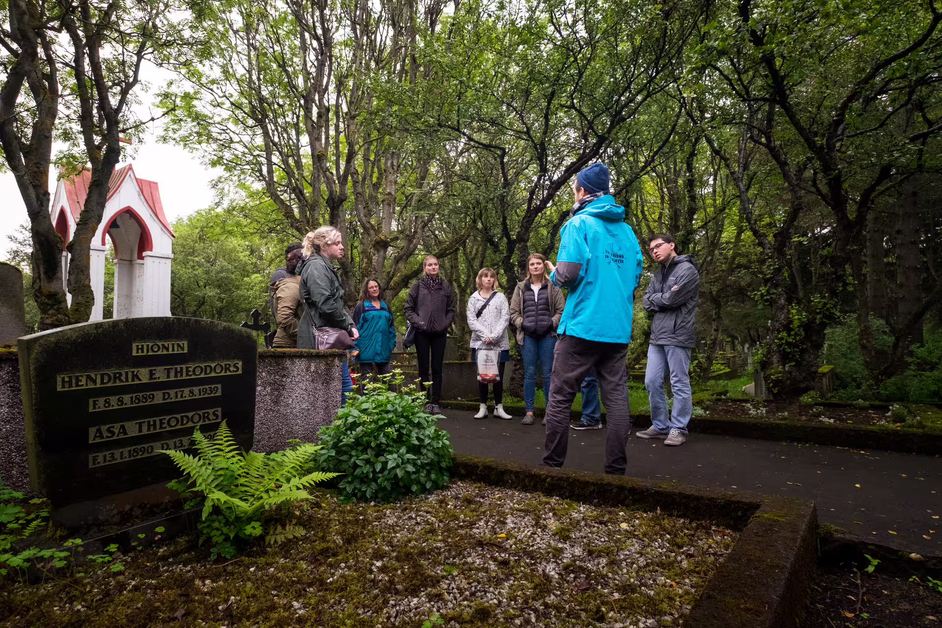 Tour guide in blue jacket leading a group through a historic Reykjavik cemetery with old gravestones
