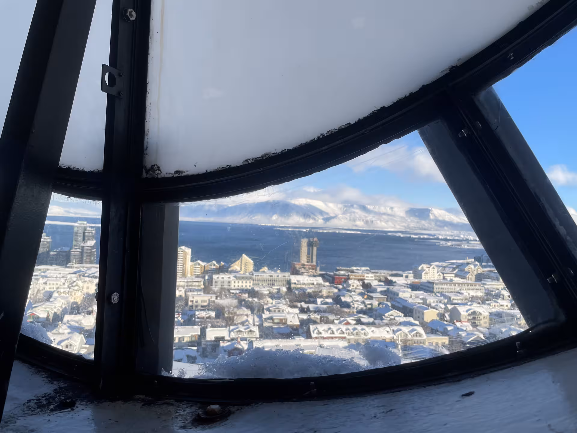 Snow-covered Reykjavik cityscape and mountains viewed through curved church tower window