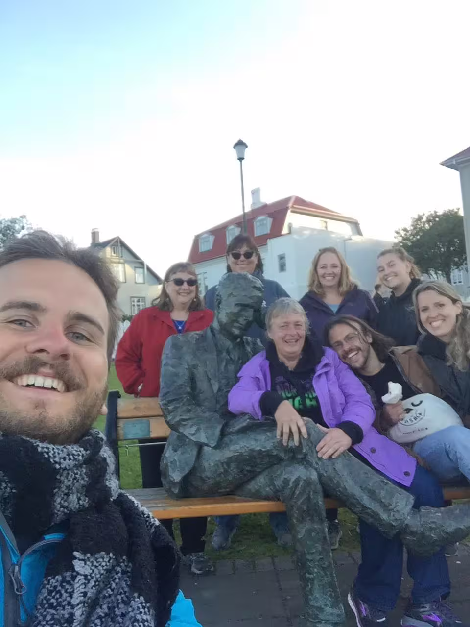 Group of tourists posing with a bronze statue on a bench during a walking tour in Reykjavik
