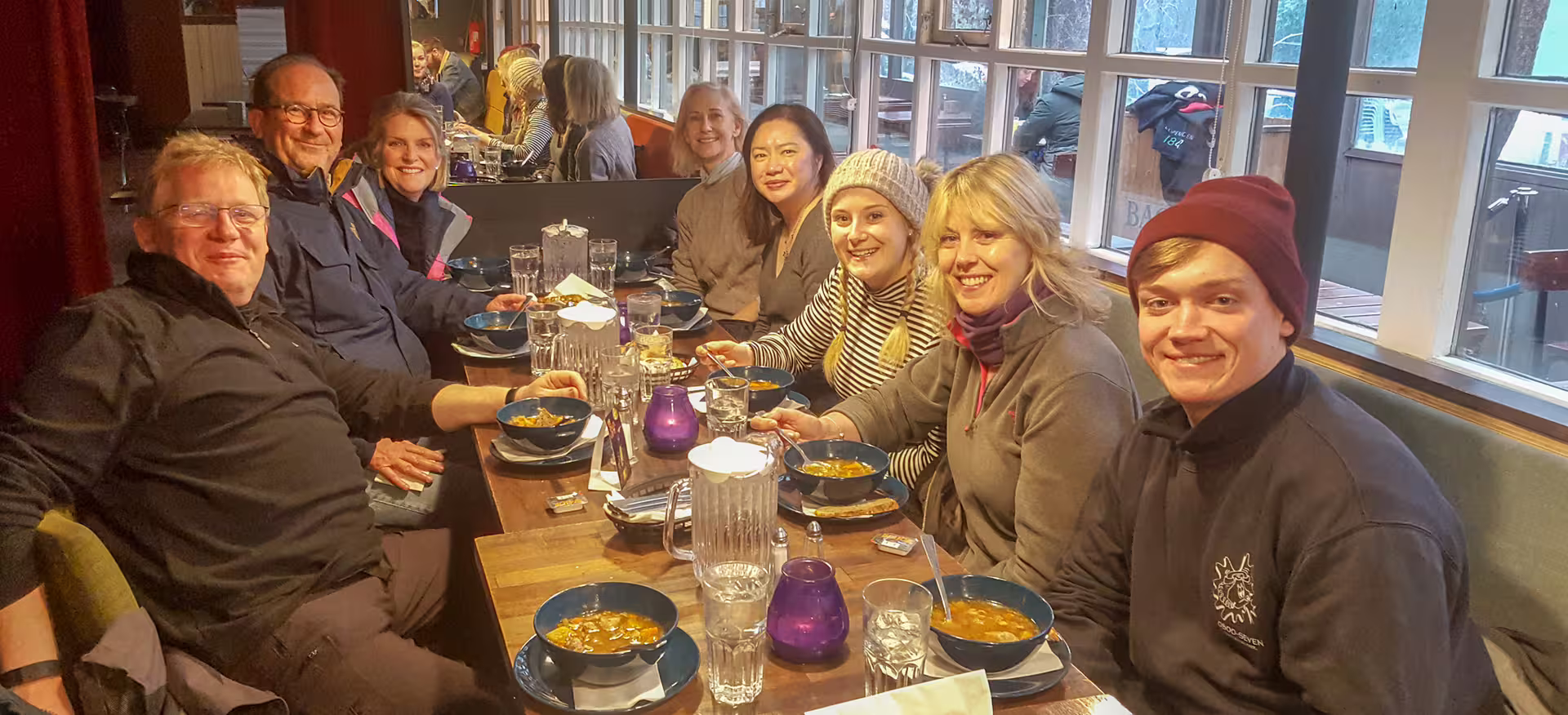 Group of eight tourists enjoying bowls of traditional Icelandic food together at a cozy Reykjavik restaurant